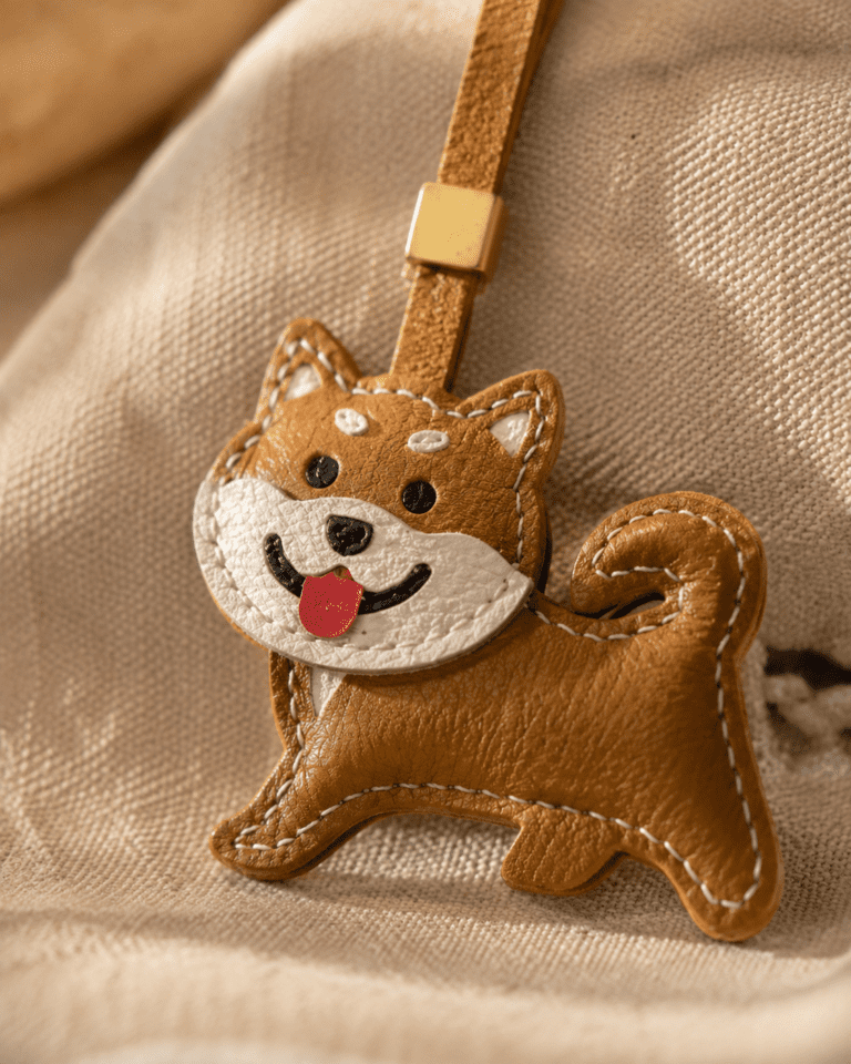 Close-up of handmade leather Shiba Inu dog charm on soft beige fabric