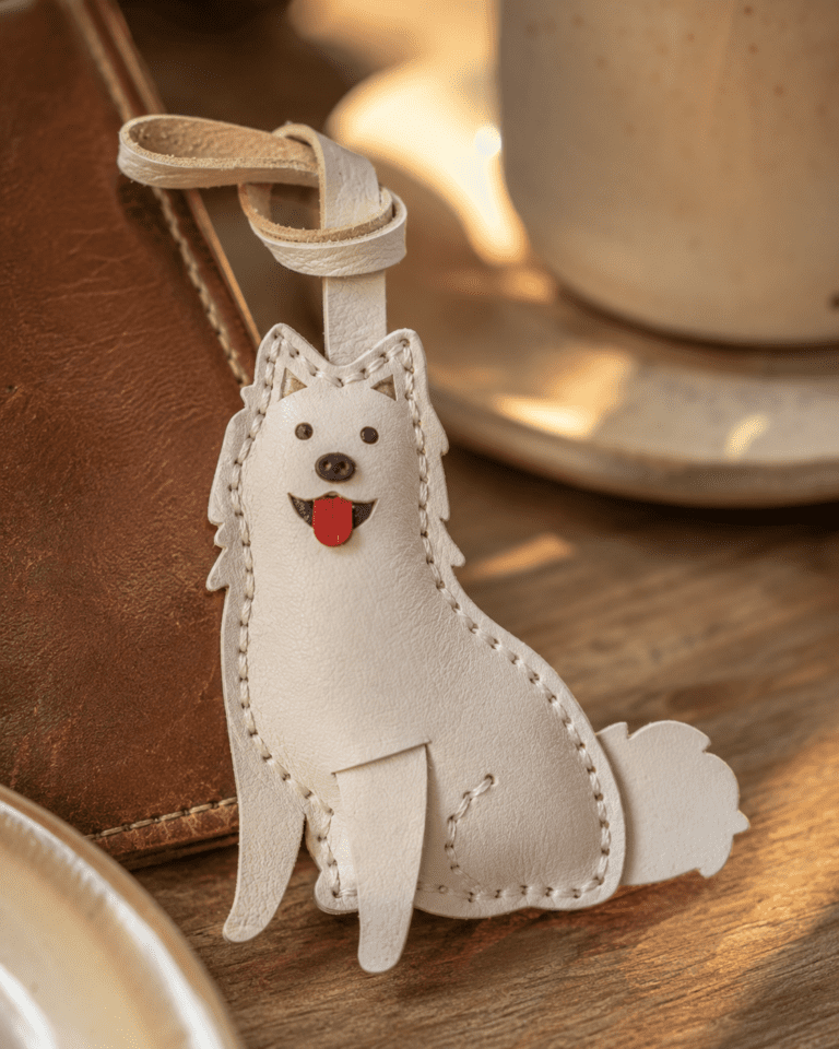 Close-up of handmade white fluffy dog leather bag charm with black eyes, black nose, red tongue, white strap, and stitched body