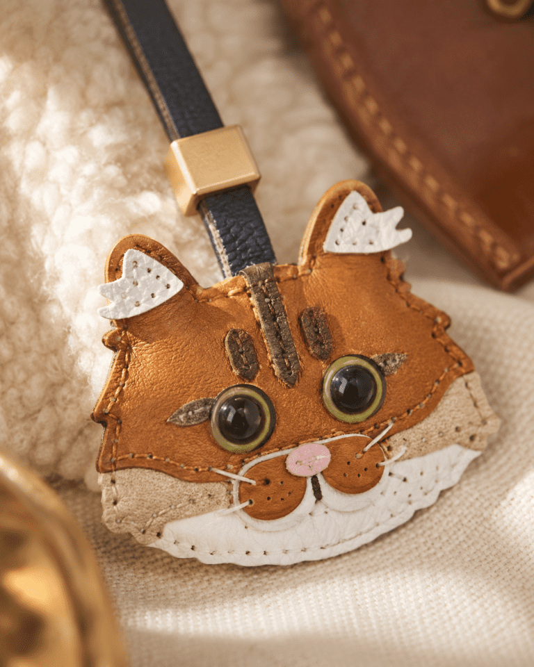 Macro photo of handmade orange tabby cat leather bag charm with green eyes, pink nose, and stitched whiskers