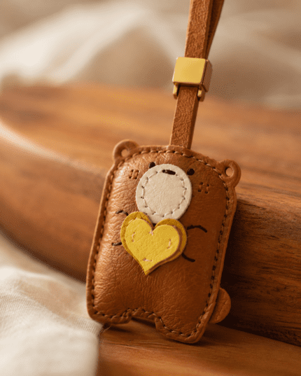 Macro photo of handmade brown bear leather bag charm with yellow heart, white muzzle, gold slider, and stitched details