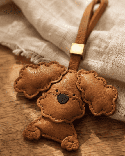 Macro photo of handmade brown poodle leather bag charm with fluffy ears, black nose, brown loop, gold slider, and stitched edges