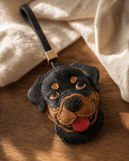 Macro photo of handmade Rottweiler leather bag charm with black and tan dog face, red tongue, black loop, gold slider, and stitched edges
