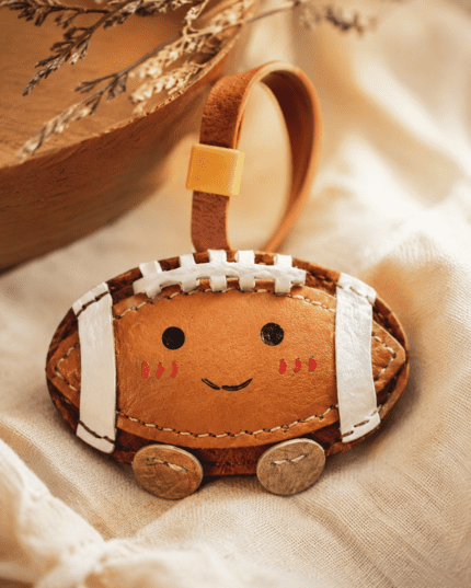 Macro photo of handmade leather football bag charm with white laces, smiling face, gold slider, and leather grain