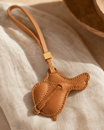Macro photo of handmade leather saddle bag charm with caramel leather, gold slider, stitching, and textured grain