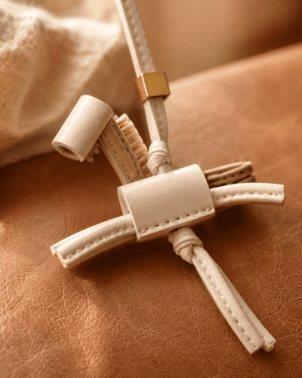 Macro photo of handmade leather toothbrush and toothpaste bag charm with cream leather, gold slider, stitching, and brush detail