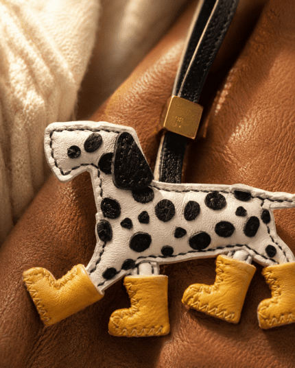 Macro photo of handmade leather Dalmatian dog bag charm with black spots, yellow boots, black strap, gold slider, and stitching