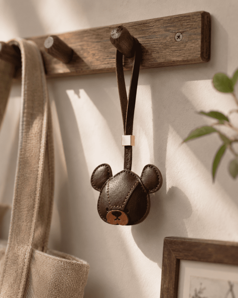 Handmade dark brown leather bear bag charm hanging from a wooden wall hook in warm sunlight