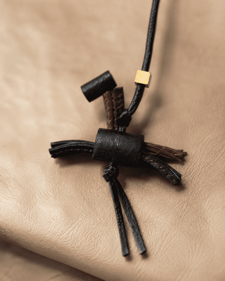 Close up of handmade black and burgundy leather tassel bag charm on a taupe leather bag