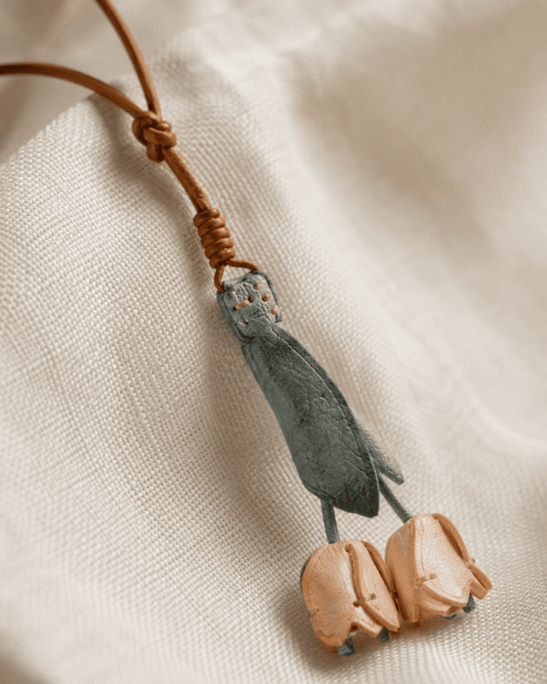 Close-up of handmade leather tulip bag charm showing sage green leather and peach tulip details