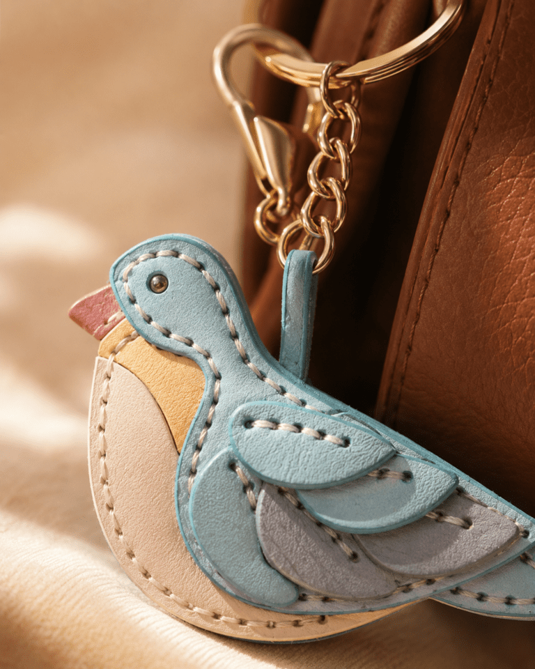 Close-up of a handmade leather blue bird bag charm with layered wings and gold chain hardware