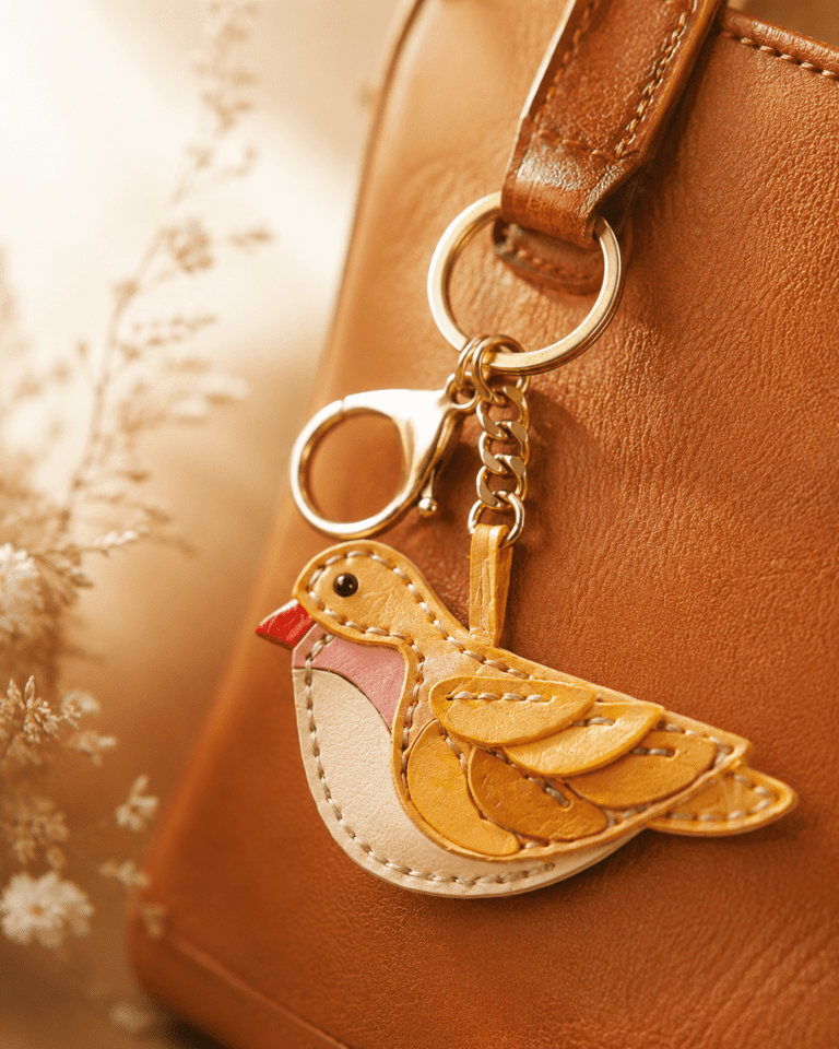 Close-up of a handmade leather yellow bird bag charm with layered wings, stitching, and gold hardware