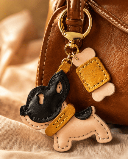 Close-up of a handmade leather black mask puppy bag charm with bone accent and gold clasp on a brown handbag