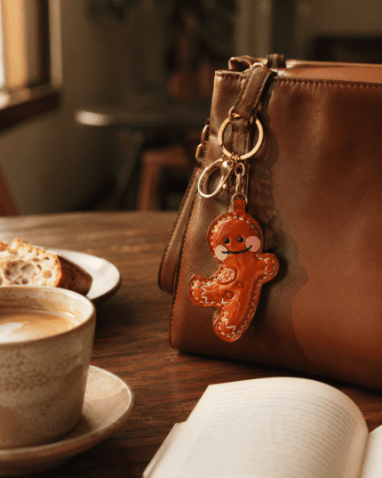 Handmade leather gingerbread man bag charm hanging on a brown leather handbag in a warm cafe scene