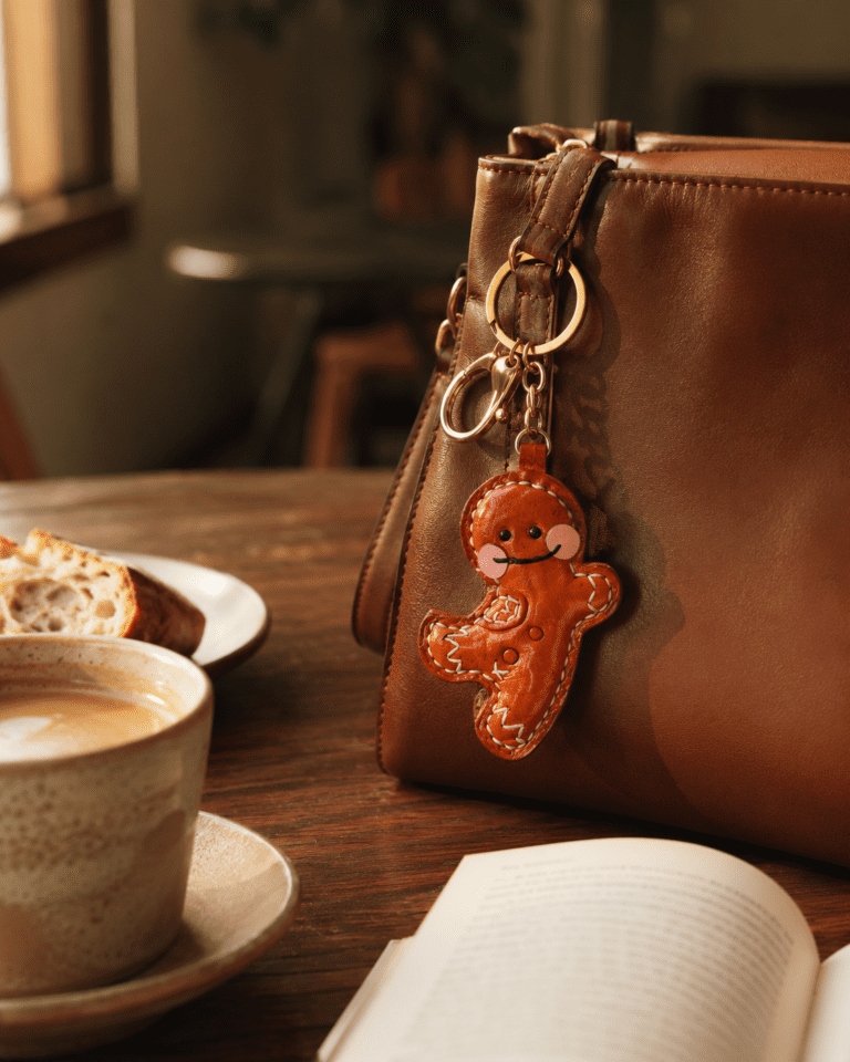 Handmade leather gingerbread man bag charm hanging on a brown leather handbag in a warm cafe scene