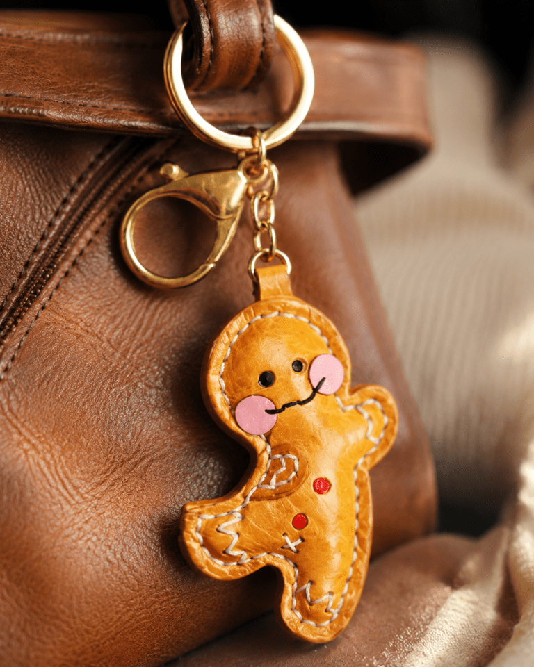 Close-up of handmade leather gingerbread man bag charm with pink cheeks, red buttons, white stitching, and gold clasp
