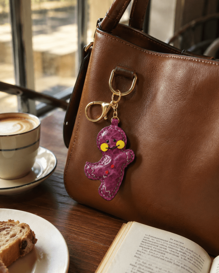 Handmade leather magenta gingerbread man bag charm hanging on a brown leather handbag in a warm cafe scene