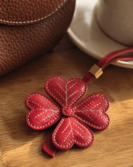 Close-up of handmade red leather four-leaf clover charm showing white stitching and pebbled leather texture