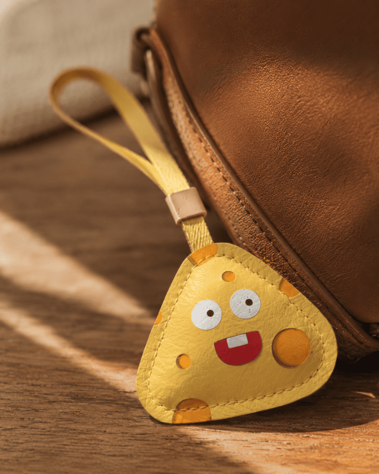 Close-up of handmade yellow cheese leather charm showing playful face, leather texture, stitching, strap, and gold slider