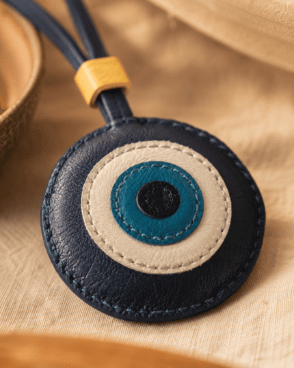 Close-up of handmade blue eye leather charm showing layered leather texture, stitching, strap, and gold slider