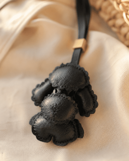 Close-up of handmade black poodle leather charm showing soft leather texture, raised shape, stitching, strap, and gold slider
