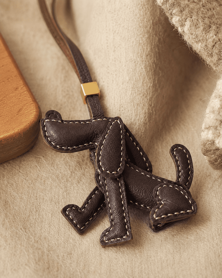 Close-up of handmade brown leather dog bag charm showing stitched edges, leather texture, strap, and gold slider