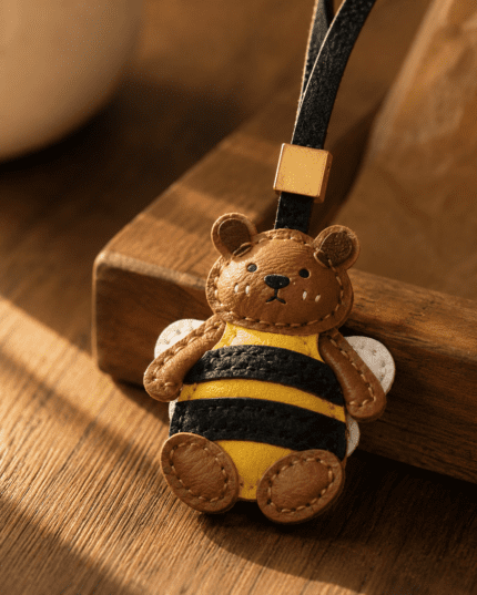 Close-up of handmade leather bear bee charm showing black strap, gold slider and stitched bee details