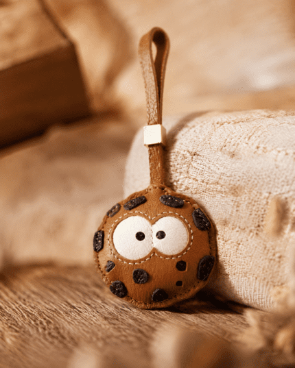 Handmade cookie leather charm on soft fabric, detailed texture and stitching close-up