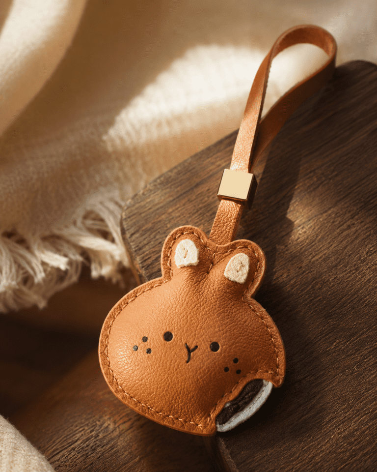 Close-up of rabbit leather bag charm with bite detail, on wooden table next to coffee and bread, warm sunlight.