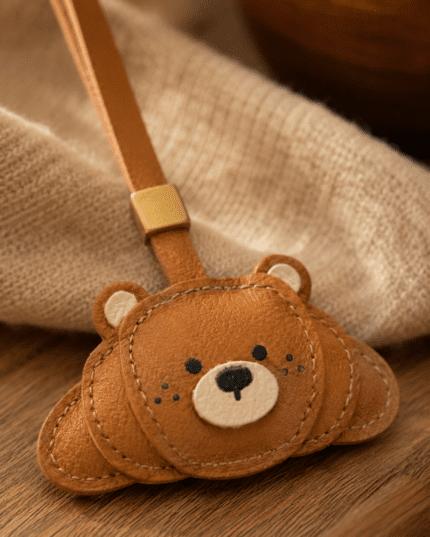 Close-up of handmade brown leather bear bag charm showing leather texture, stitched bear face, cream muzzle, and gold slider.