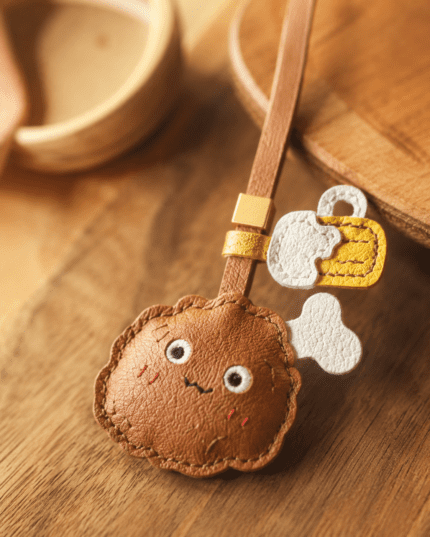 Close-up of handmade leather fried chicken and beer bag charm showing brown leather texture, cute face, white bone, yellow beer detail, stitching, and gold slider.