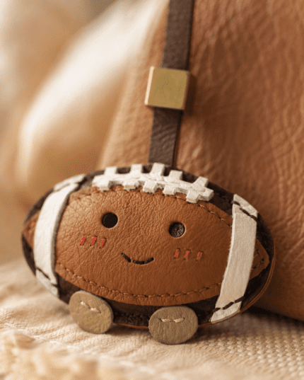 Handmade leather football bag charm on brown leather handbag, cozy café setting with coffee and book