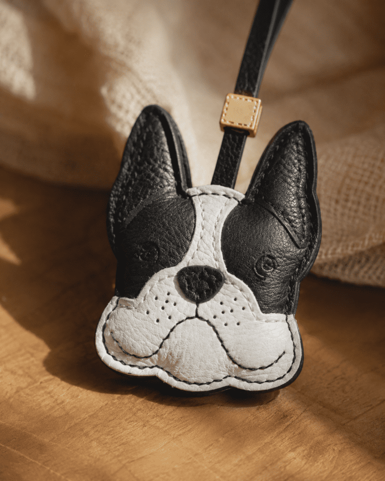 Close-up of handmade French bulldog leather bag charm showing black ears, white face, stitched nose, and leather texture